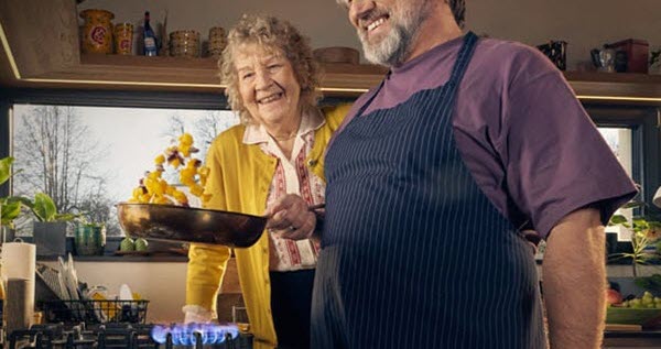 Dekoratives Bild Ein älteres Ehepaar steht gemeinsam vor dem Gasherd. Der Mann hält eine Pfanne in der Hand und schwingt das Essen.